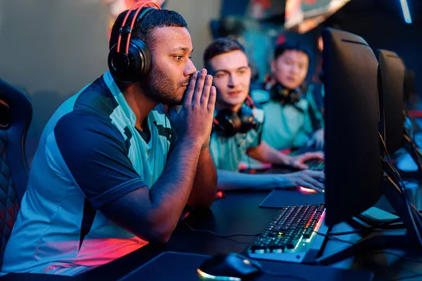 A small crew of players sharing a bank of stations under teal and red light