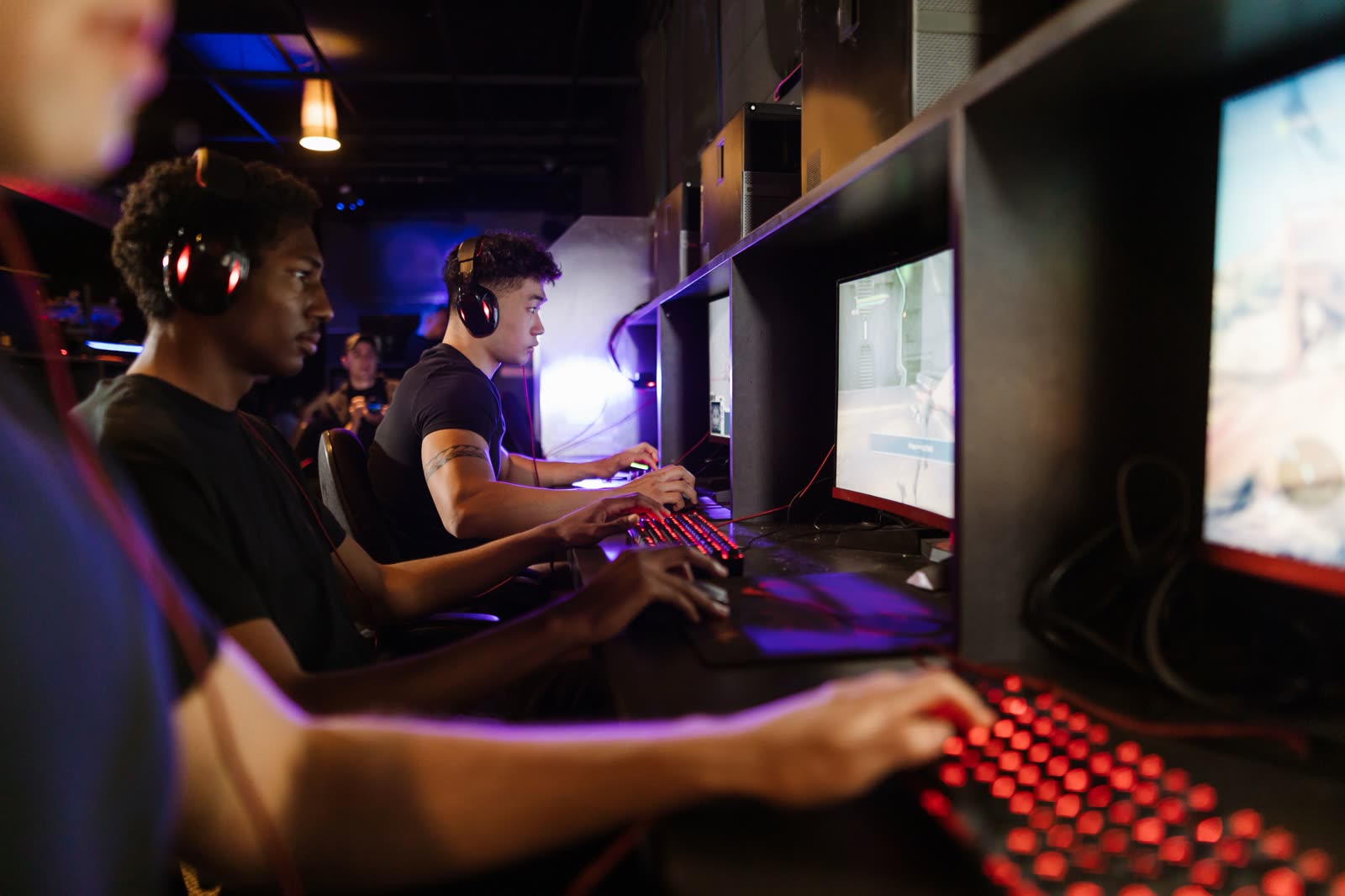 A close crew of players at glowing red keyboards under a row of monitors